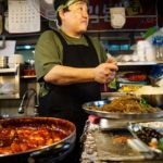Seoul, South Korea: Cook at a street food stall with noodles and sushi in Gwanjang Market