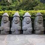 Six Dol Hareubang statues in a line in green forest, Seogwipo, Jeju Island, South Korea