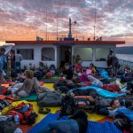 Passengers on mats and luggage on the deck of a ferry from Wakai to Gorontalo, Sulawesi, Indonesia, during sunrise with red colored clouds
