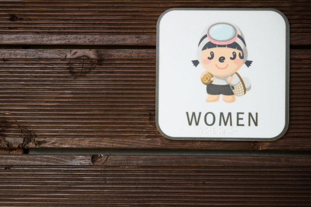 Manga comic logo of the Haenyeo woman with mask on a toilet sign on a wooden wall