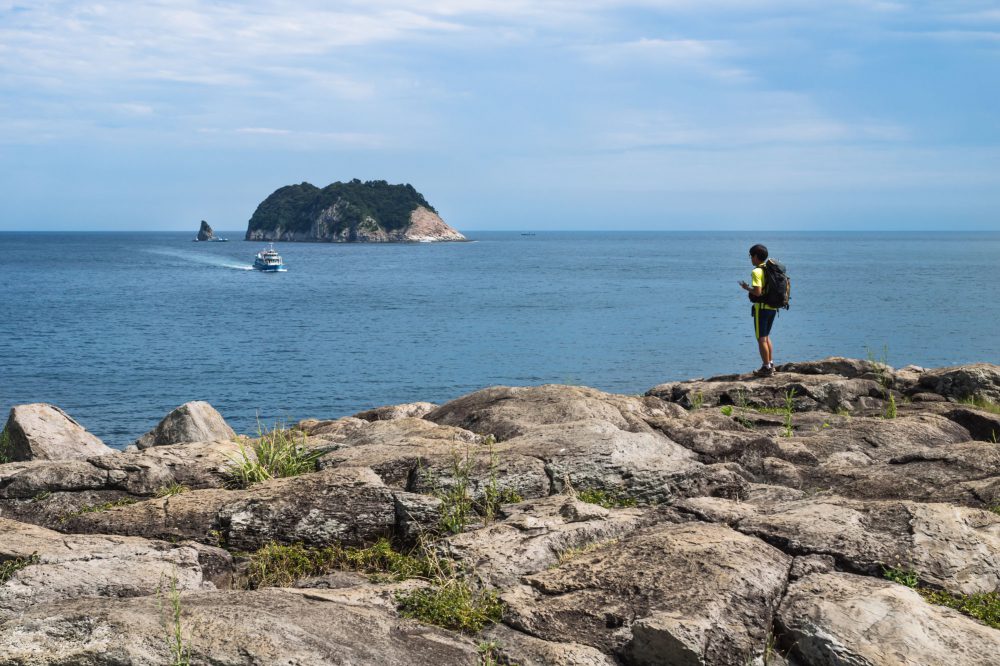 Hiker on a stone cliff with view to ocean and Moon Island, Seogwipo, Jeju Island, South Korea