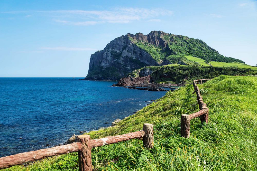 Volcano crater Ilchulbong along the ocean and the green coastline with a fence in Seongsan, Jeju Island, South Korea