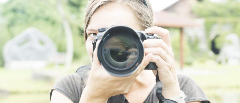 | ABOUT | woman behind large camera in green park