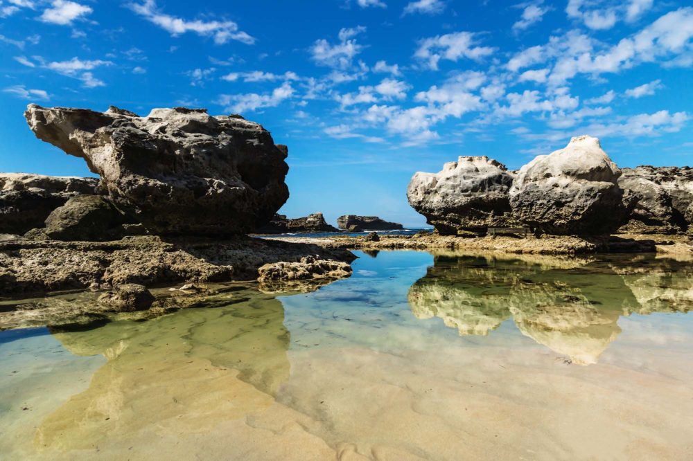 Three rock formations with reflections in the sea at Peterborough beach, Victoria, Australia