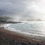 Puerto de la Cruz, Tenerife, Canary Islands, Black beach with people along the ocean with sunrays lightening the village and mountainrange, Spain