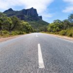 Asphalt road leading to the Grampians rocky mountains lined by trees, Victoria, Australia